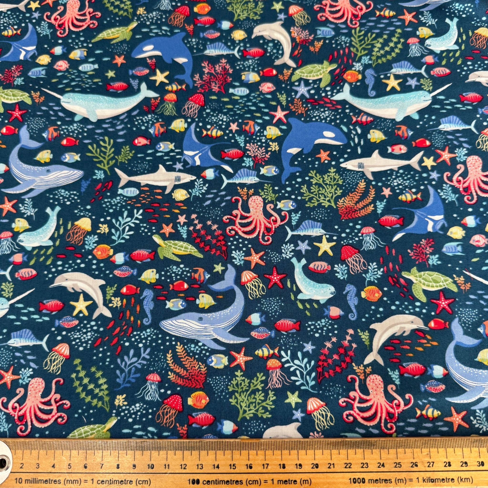 Underwater-themed fabric with various sea creatures on a blue background, accompanied by a ruler for scale.