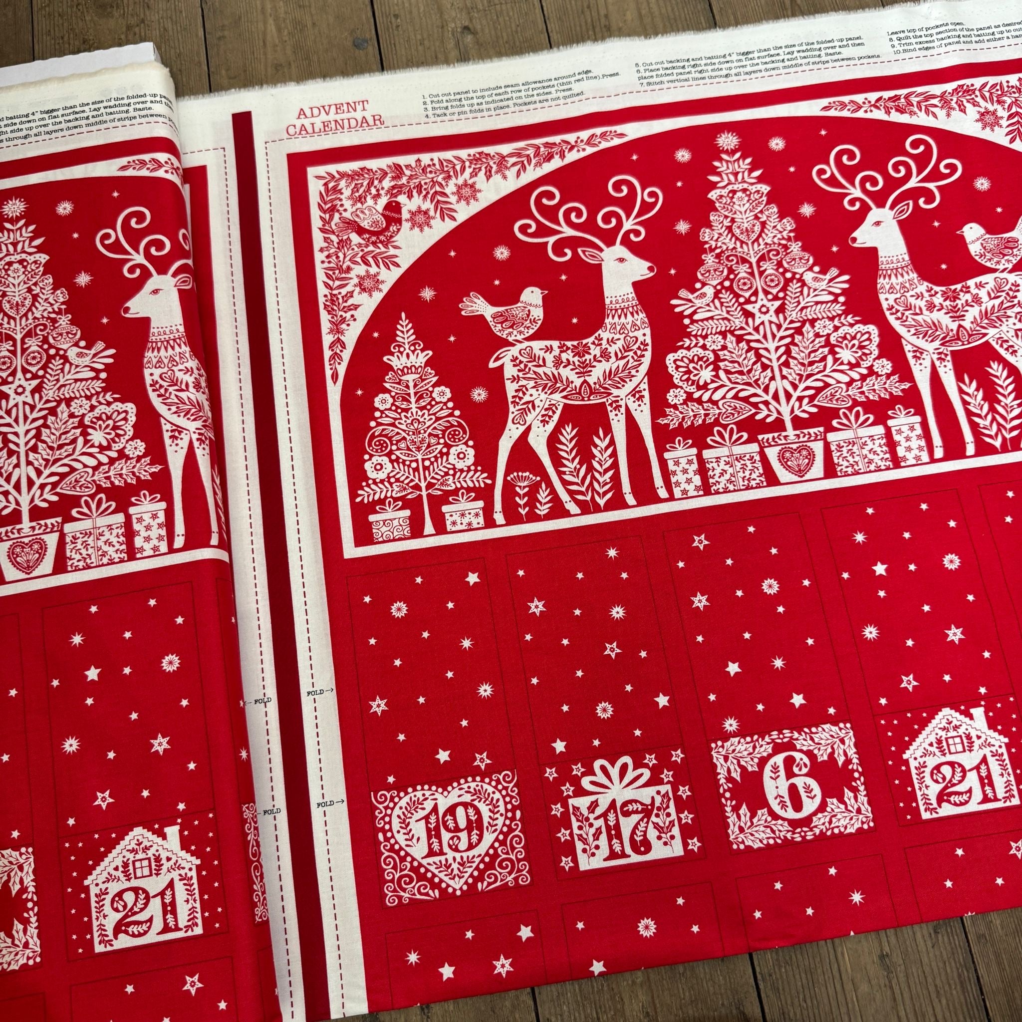 Red and white Christmas-themed fabric with reindeer, trees, and numbers on a wooden surface