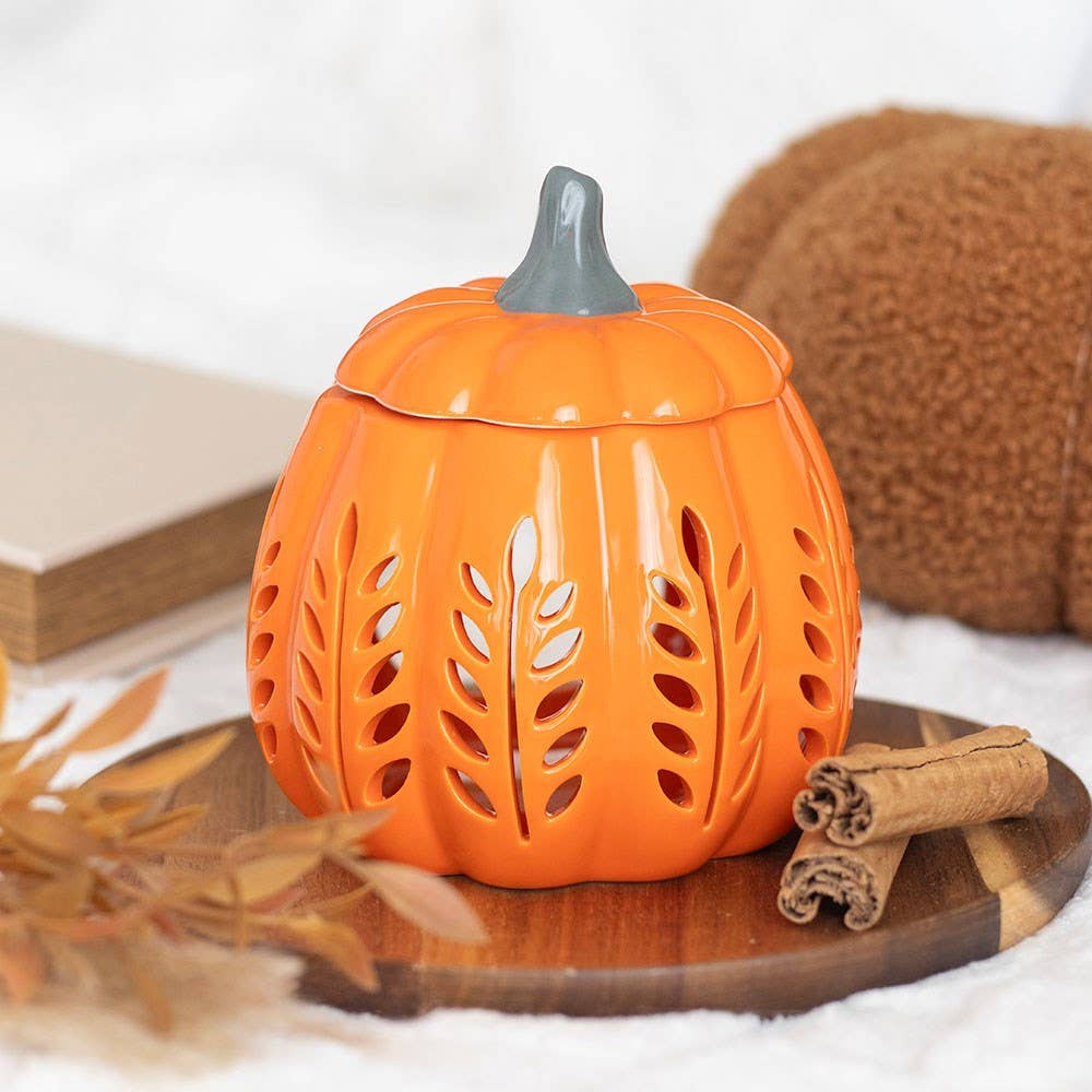 Pumpkin-shaped lantern with cut-out designs on a wooden surface with cinnamon sticks and a book in the background.