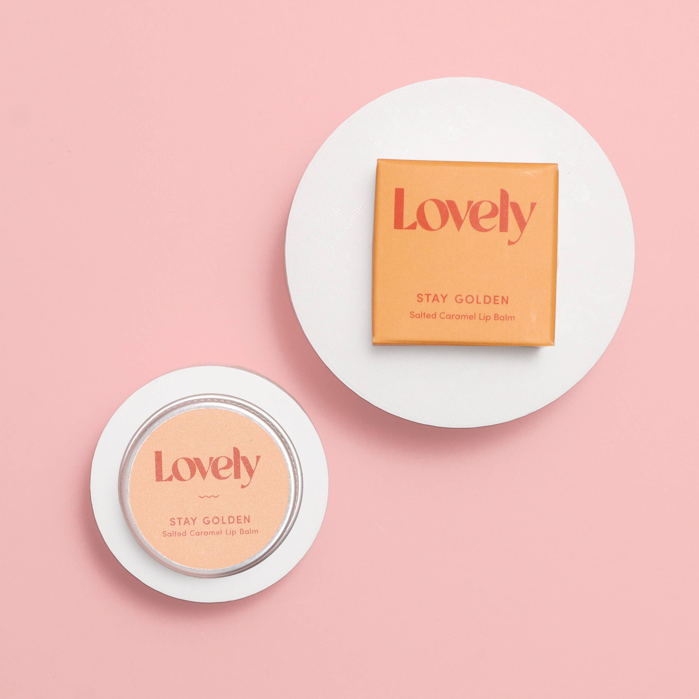 Two 'Lovely' lip balm containers on a pink background