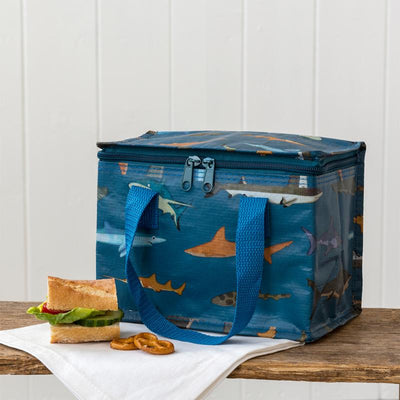 Blue insulated lunch bag with shark design on a wooden surface with a sandwich and pretzels.