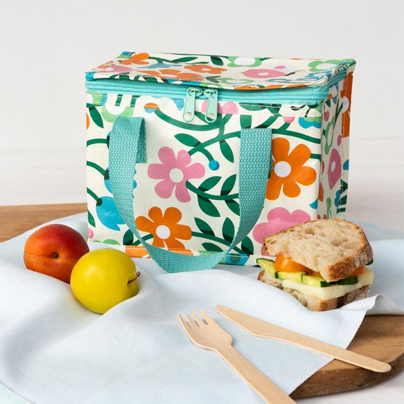Floral-patterned lunch bag with a sandwich, fruit, and cutlery on a white surface