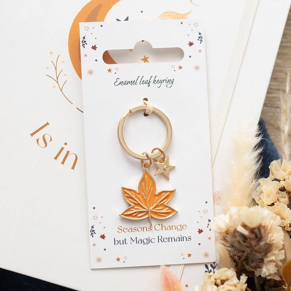 Gold leaf keychain on a decorative card with autumn-themed text and elements.