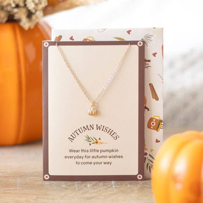 Necklace with a pumpkin charm on an 'Autumn Wishes' card, surrounded by pumpkins.