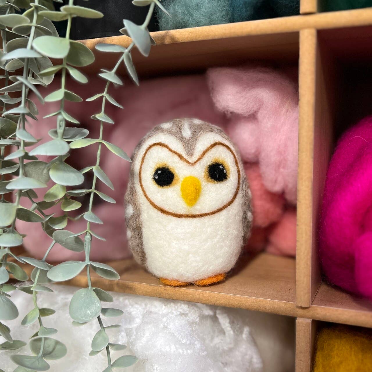 Felted owl toy on a wooden shelf with pink and green elements