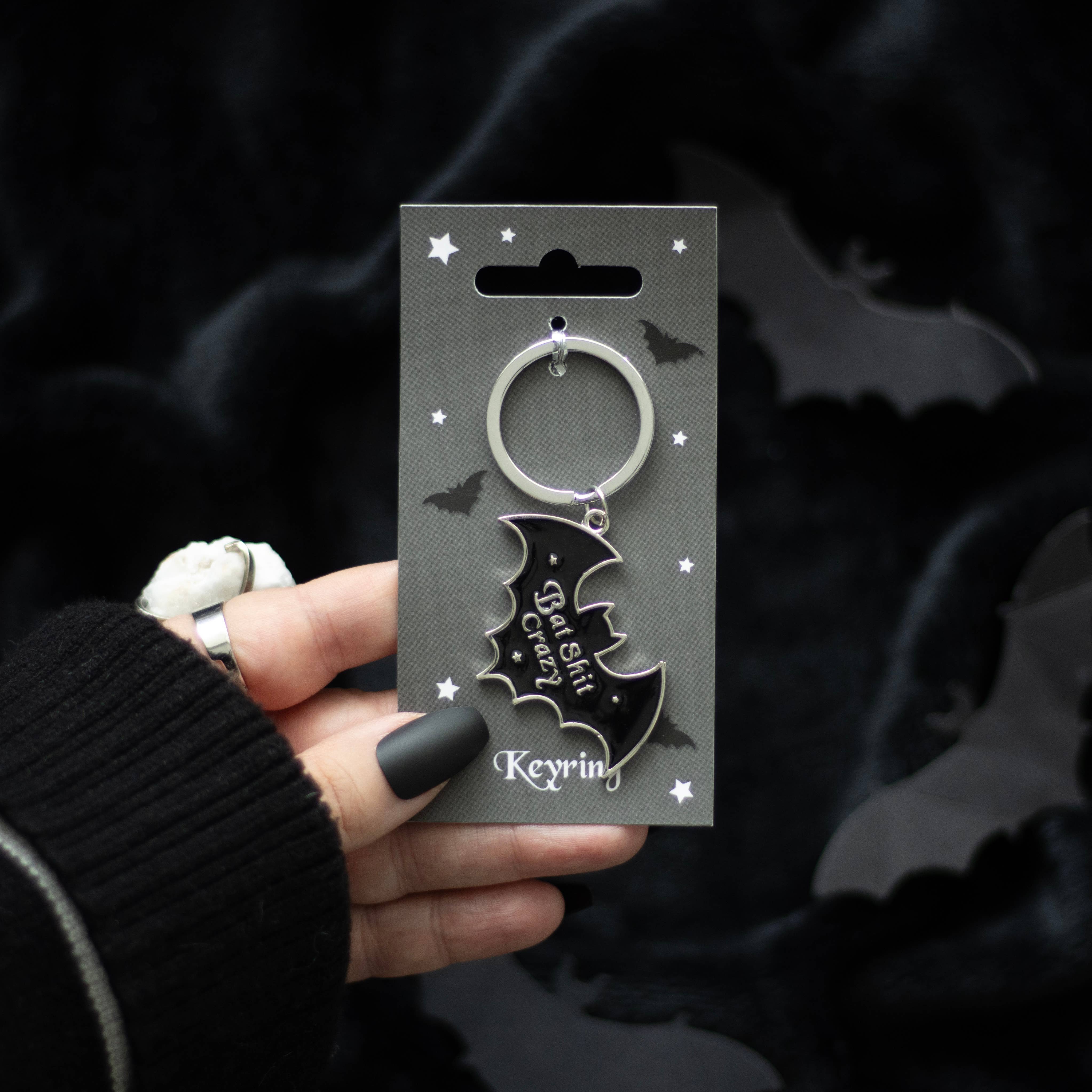 Keychain with bat design held by a hand against a dark background with bats.