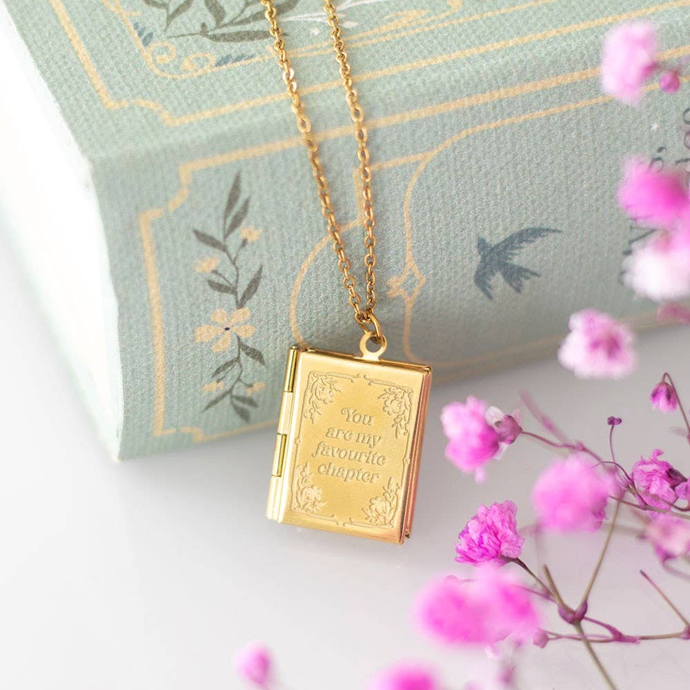 Gold locket necklace with floral design on a light blue pillow with pink flowers.