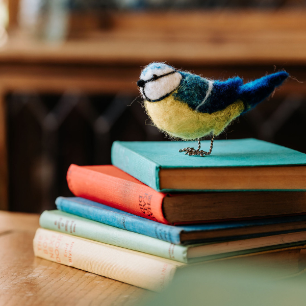 Felted bird toy perched on a stack of colorful books with a blurred background