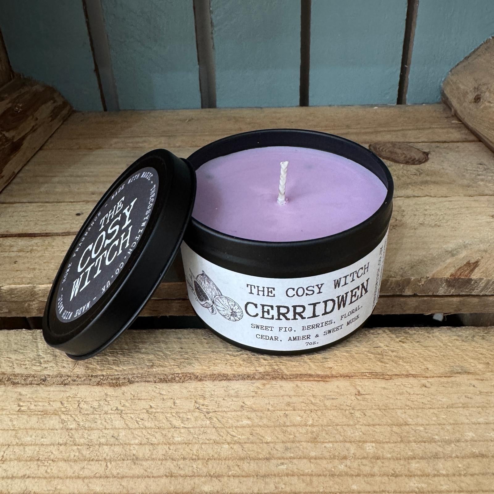 Candle in a container labeled 'The Cosy Witch Cerridwen' on a wooden surface.