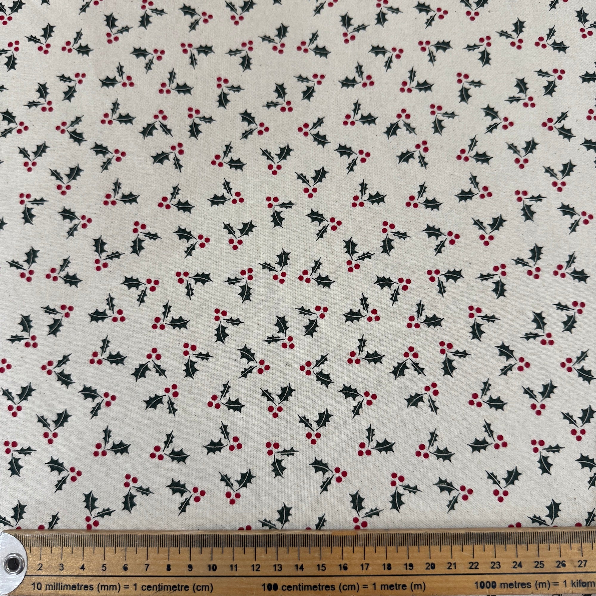 Fabric with holly berry pattern and a ruler for scale on a white background