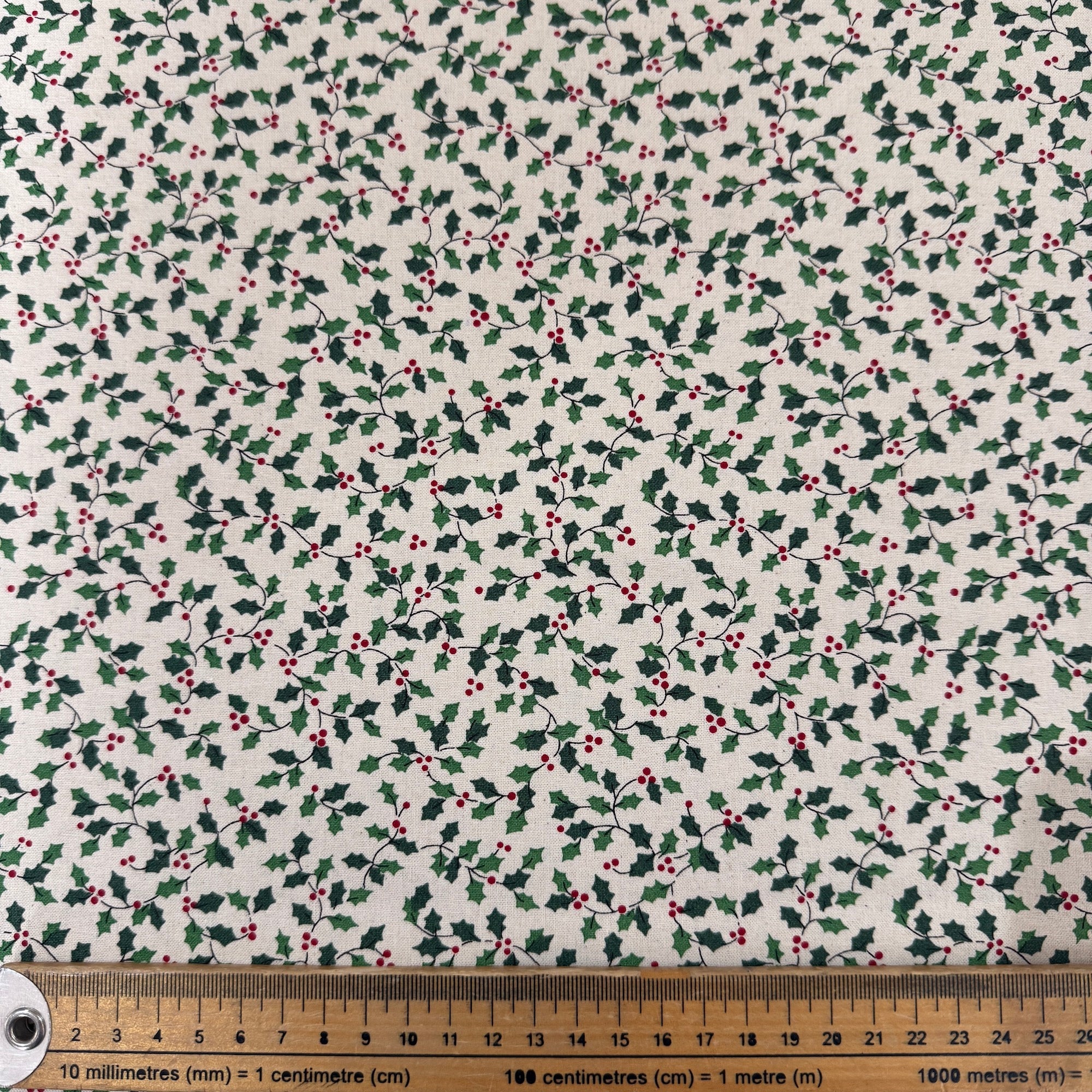 Fabric with holly berry pattern on a white background, ruler at the bottom for scale.