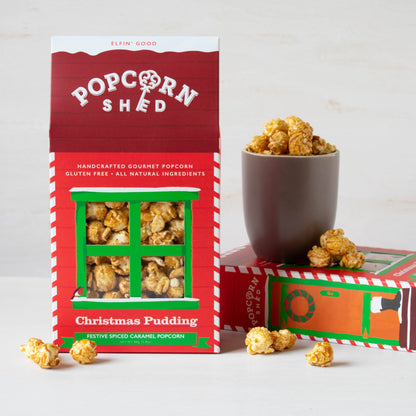 Popcorn Shed Christmas Pudding popcorn packaging with a cup of popcorn on a light background