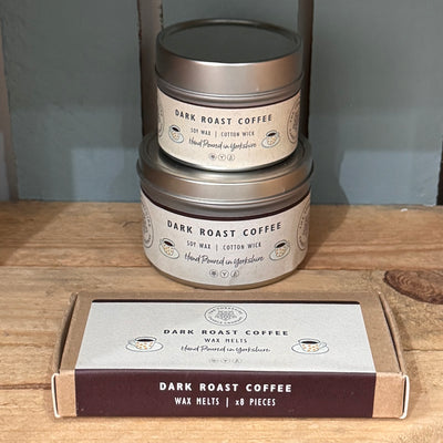 Two tins of 'Dark Roast Coffee' wax melts on a wooden surface with a gray background.