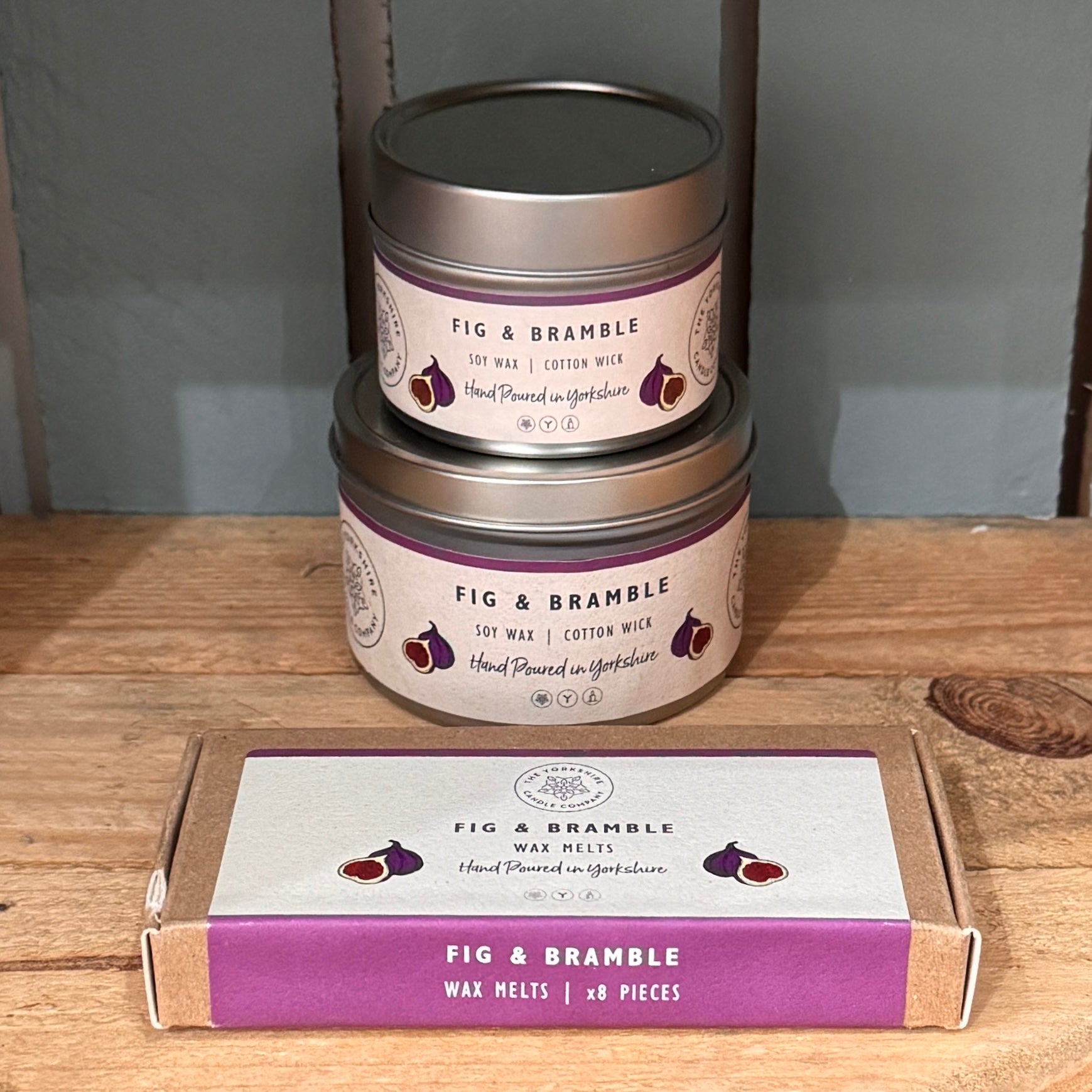 Two candles and a box of wax melts with 'Fig & Bramble' branding on a wooden surface.