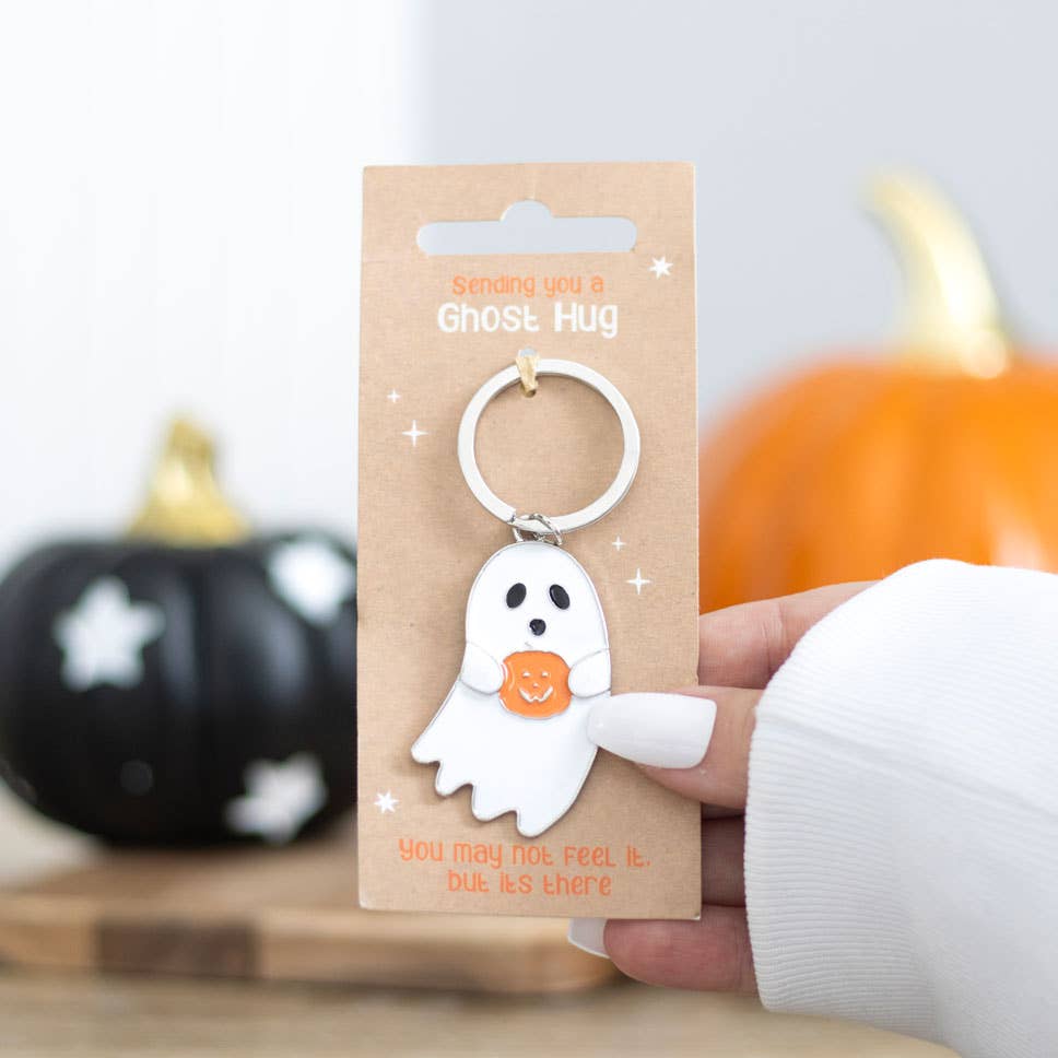 Halloween-themed ghost keychain on a cardboard backing with pumpkins in the background