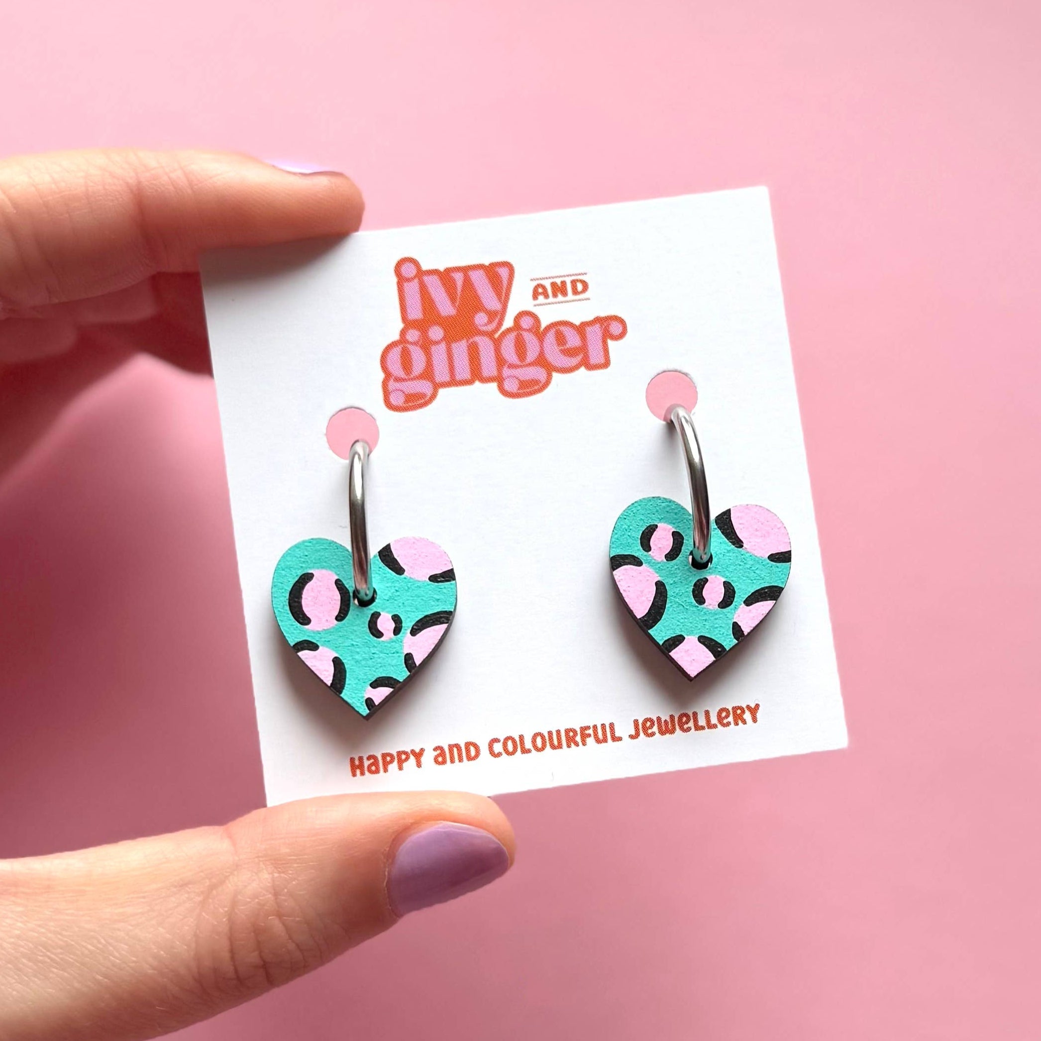 Heart-shaped earrings on a 'ivy and ginger' branded card against a pink background