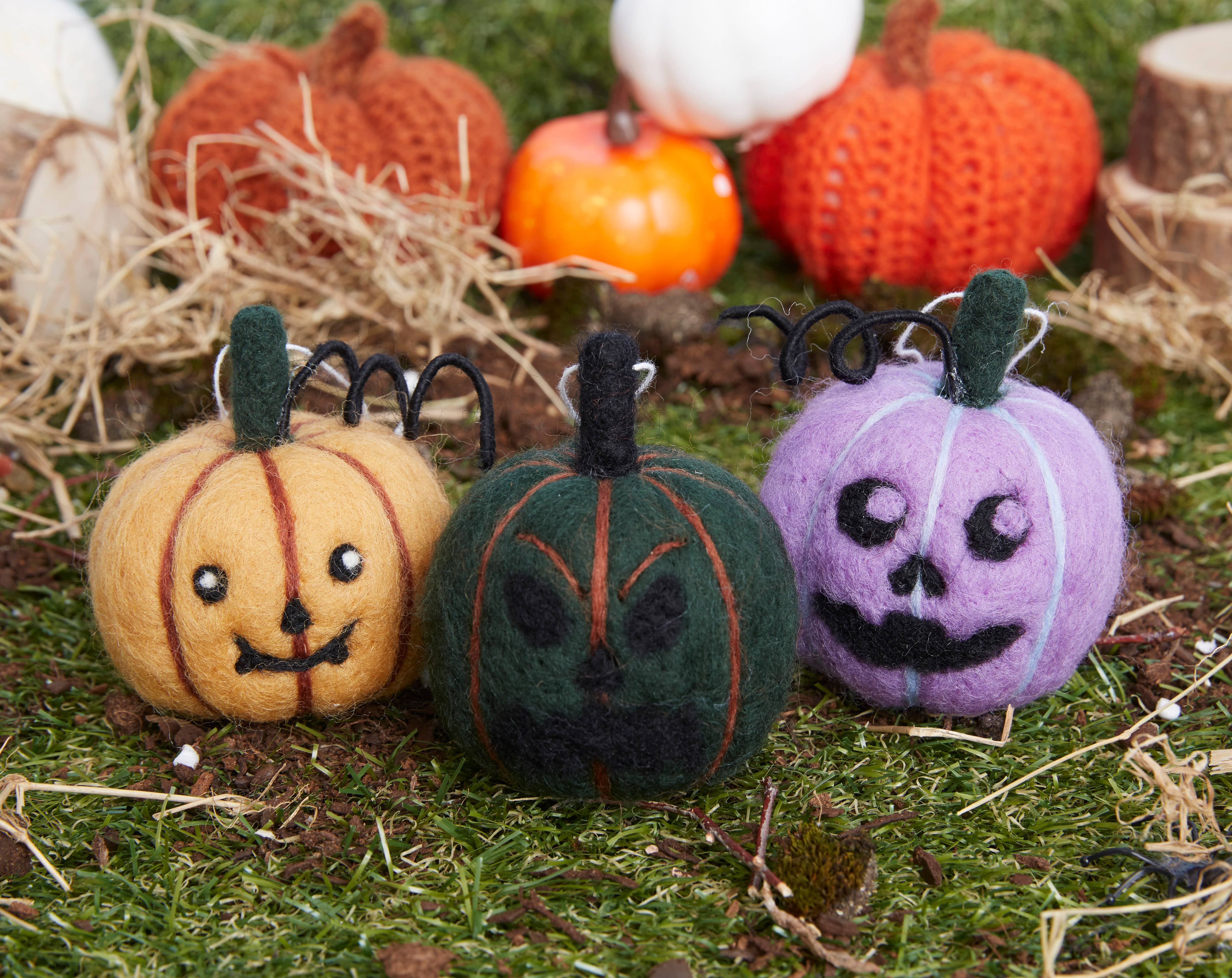 Three felt pumpkins with black wire stems on a grassy background with small pumpkins.