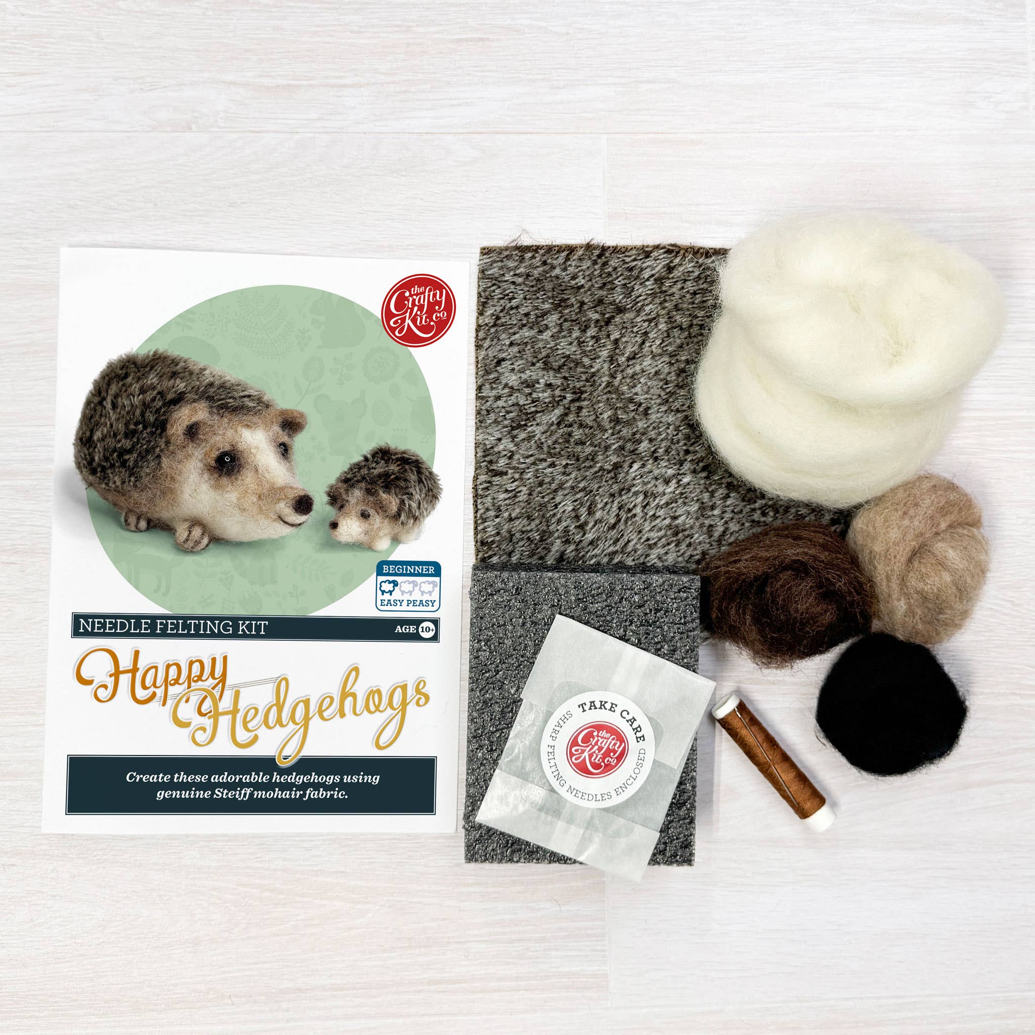 Craft kit for needle felting hedgehogs with felt squares, yarn, and tools on a white background.