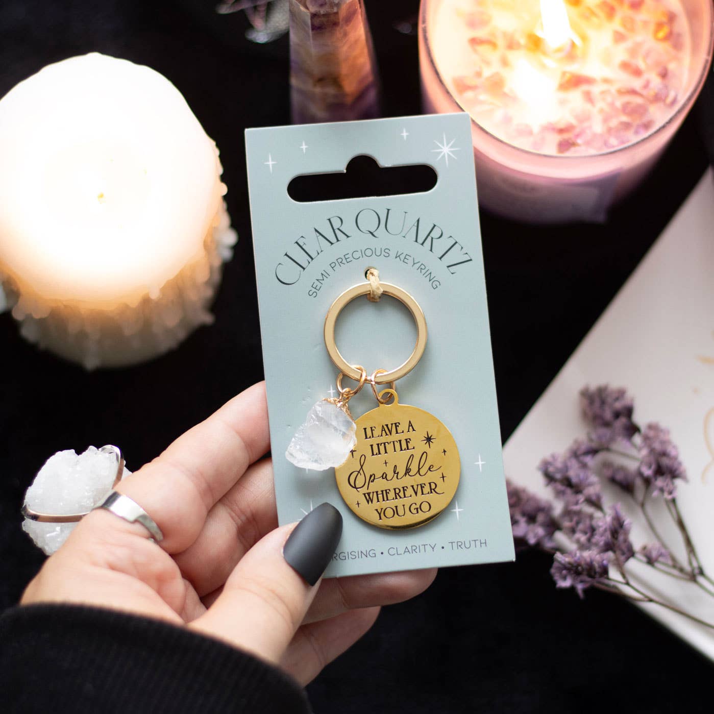 Clear Quartz keychain on packaging with a hand holding it, candles, and crystals in the background.