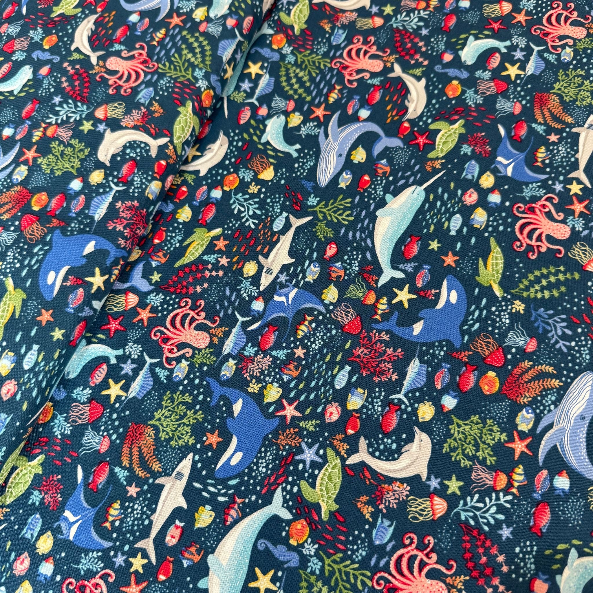 Colorful ocean-themed fabric pattern with whales, dolphins, and sea creatures on a dark blue background.