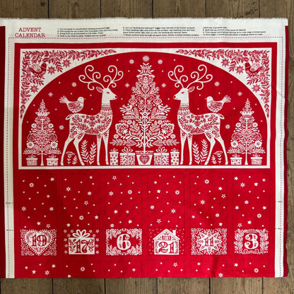 Red and white Christmas-themed advent calendar with reindeer and trees on a wooden surface.