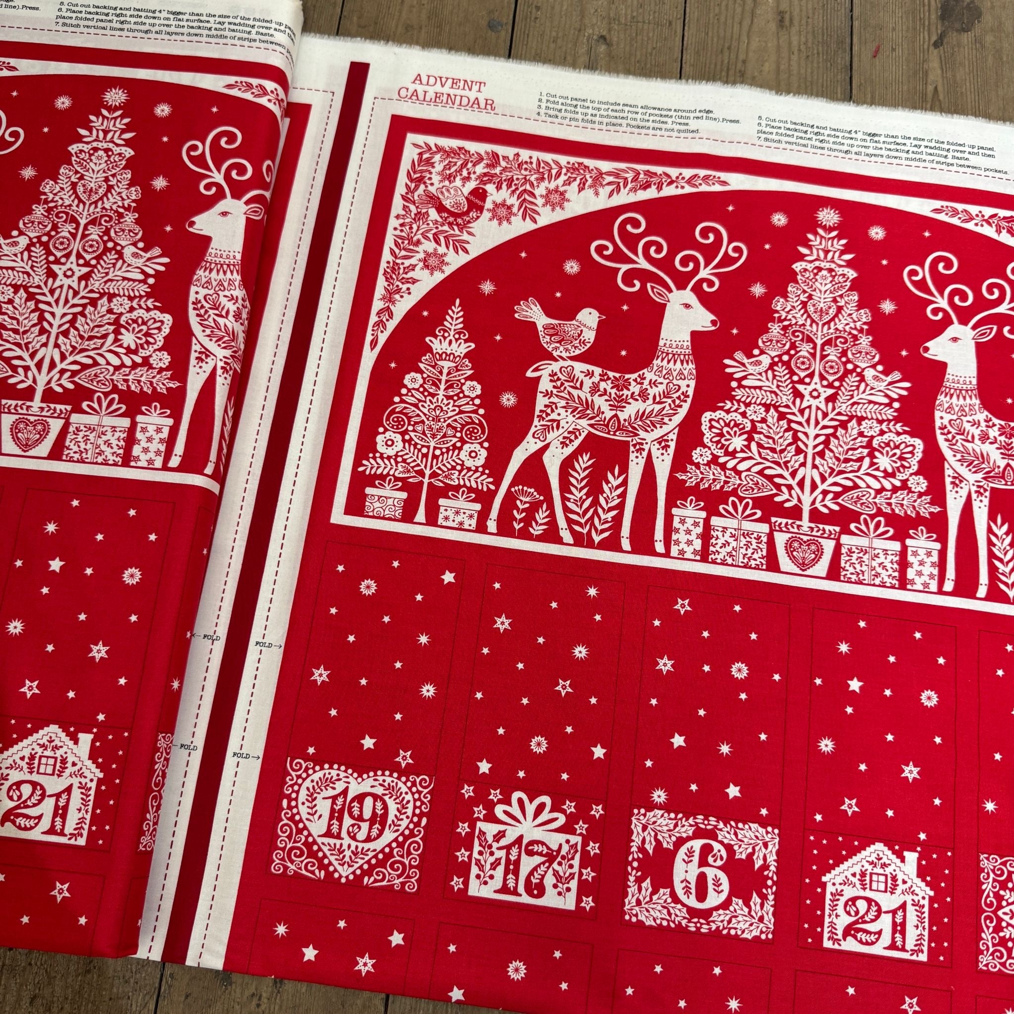 Red and white Christmas-themed fabric with reindeer, trees, and numbers on a wooden surface