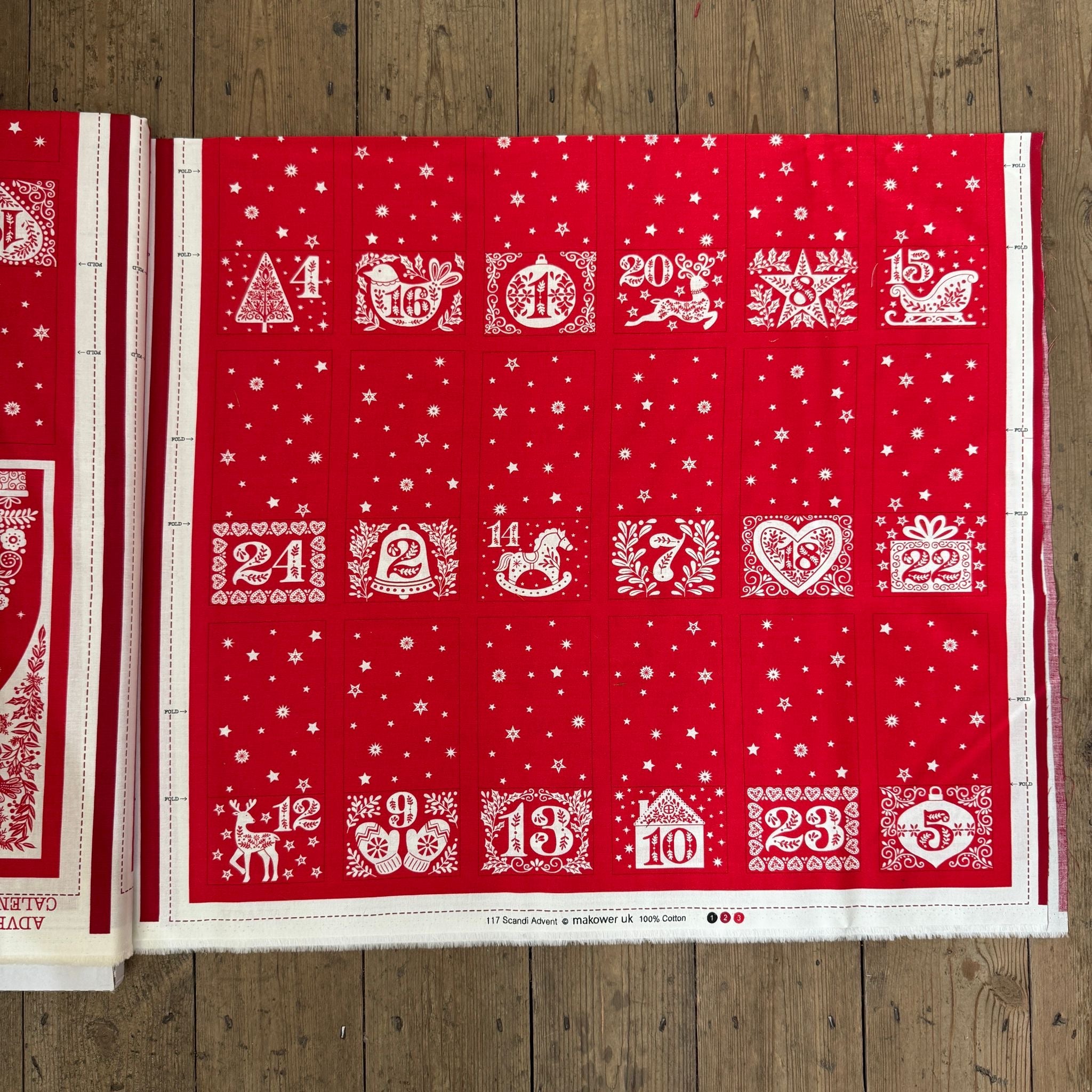 Red advent calendar with white designs and numbers on a wooden surface
