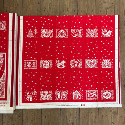 Red advent calendar with white designs and numbers on a wooden surface