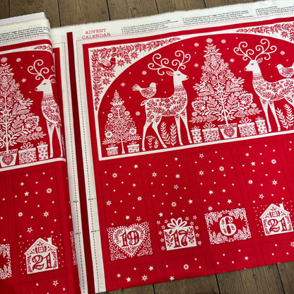 Red and white Christmas-themed fabric with reindeer, trees, and numbers on a wooden surface