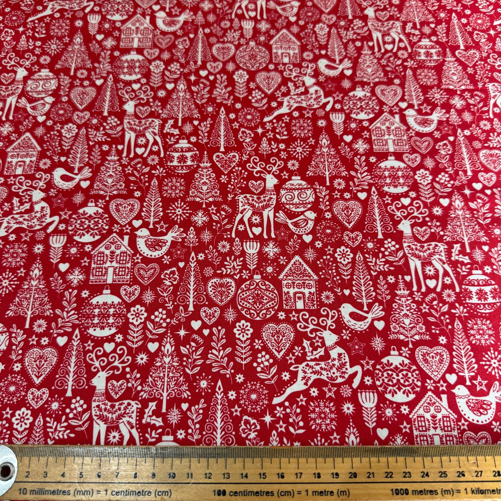 Red fabric with white Christmas-themed patterns including reindeer, trees, and houses.