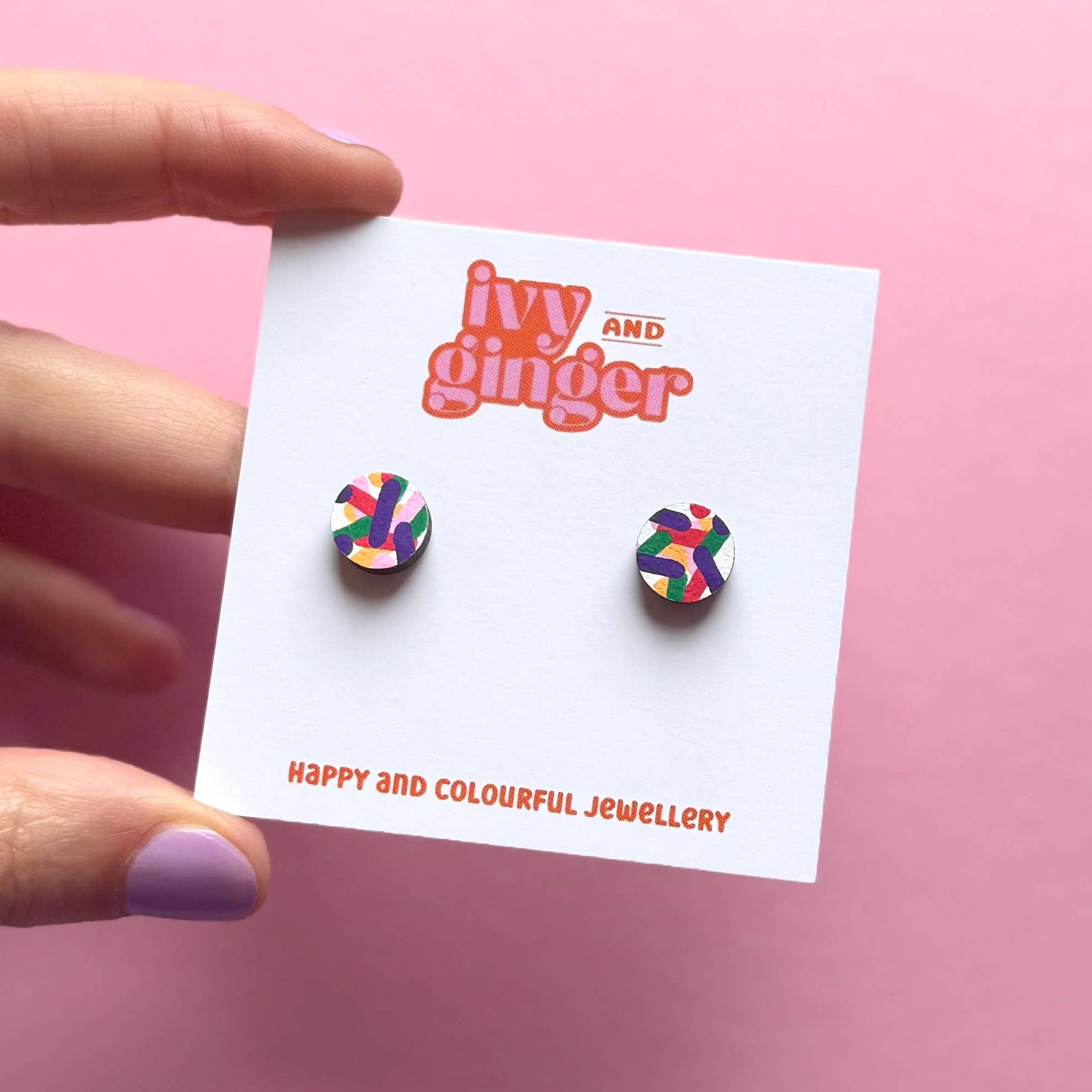 Colorful earrings on a 'ivy and ginger' branded card against a pink background