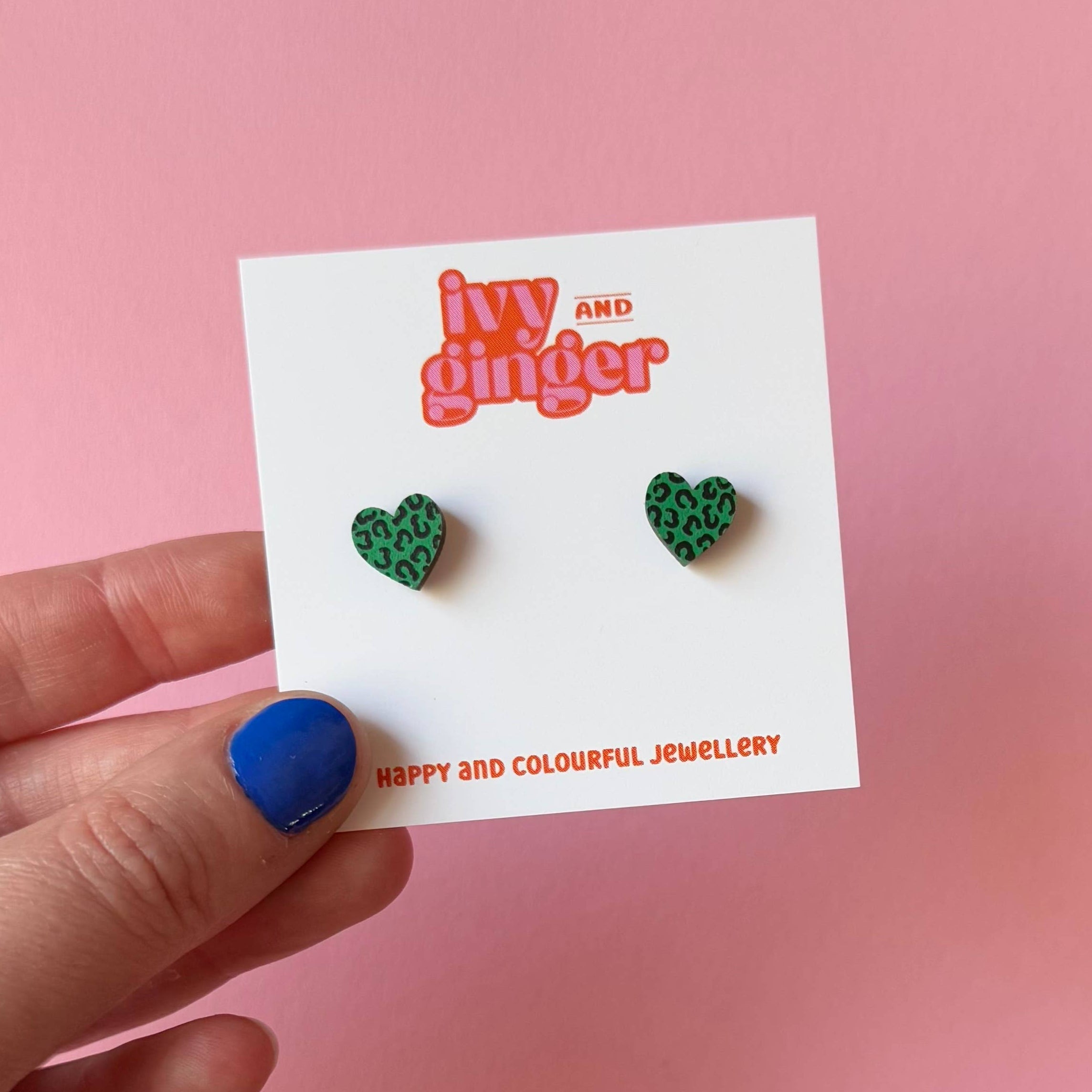 Green heart-shaped earrings on a 'Ivy and Ginger' branded card against a pink background.
