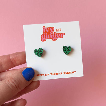 Green heart-shaped earrings on a 'Ivy and Ginger' branded card against a pink background.