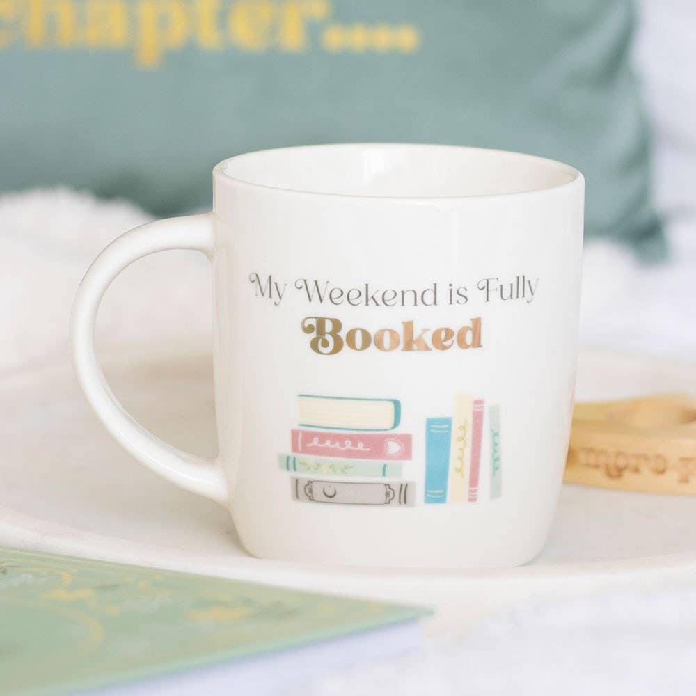 White mug with 'My Weekend is Fully Booked' text and book illustrations on a light background
