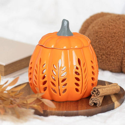 Pumpkin-shaped lantern with cut-out designs on a wooden surface with cinnamon sticks and a book in the background.