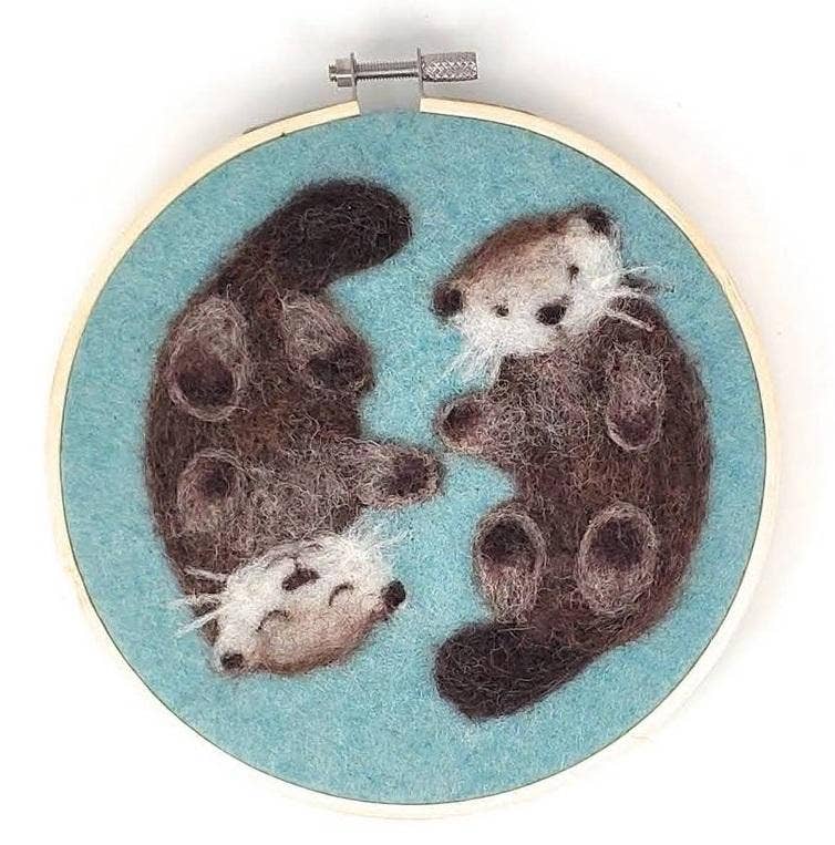Embroidery hoop with two felted otters on a blue background