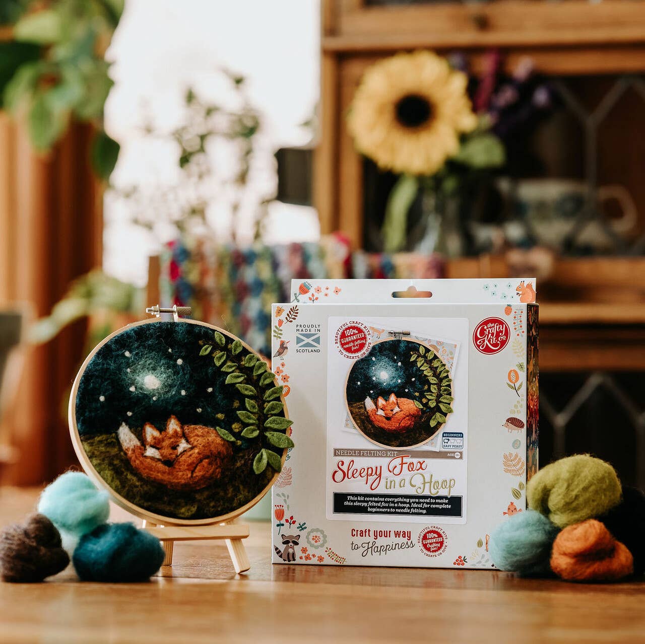 Embroidery hoop with a fox design and craft kit packaging on a wooden table.
