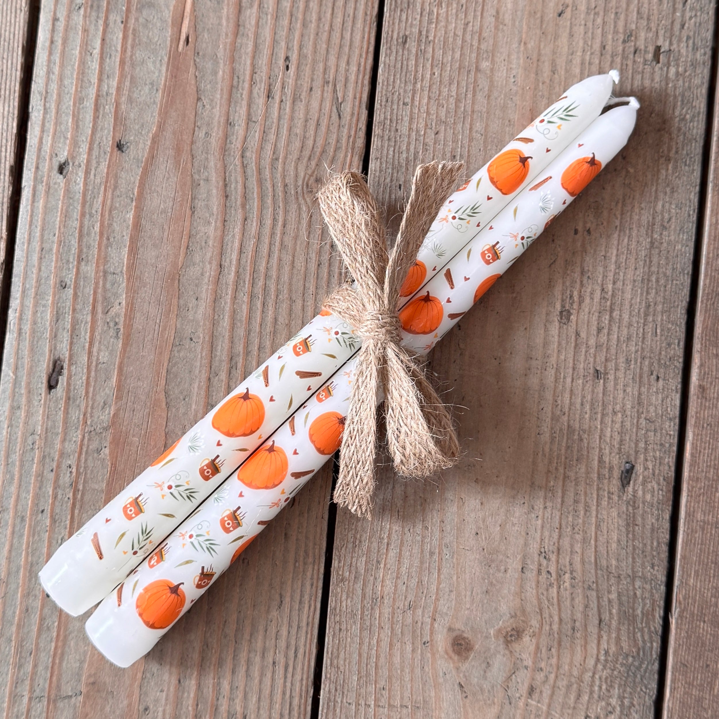 Decorative candles with pumpkin pattern tied with twine on a wooden surface