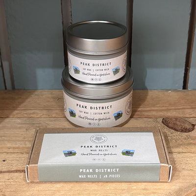 Two stacked tins and a box of Peak District products on a wooden surface.