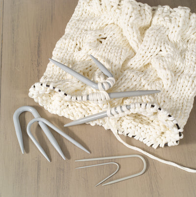 Knitted white fabric with U shaped needles on a wooden surface