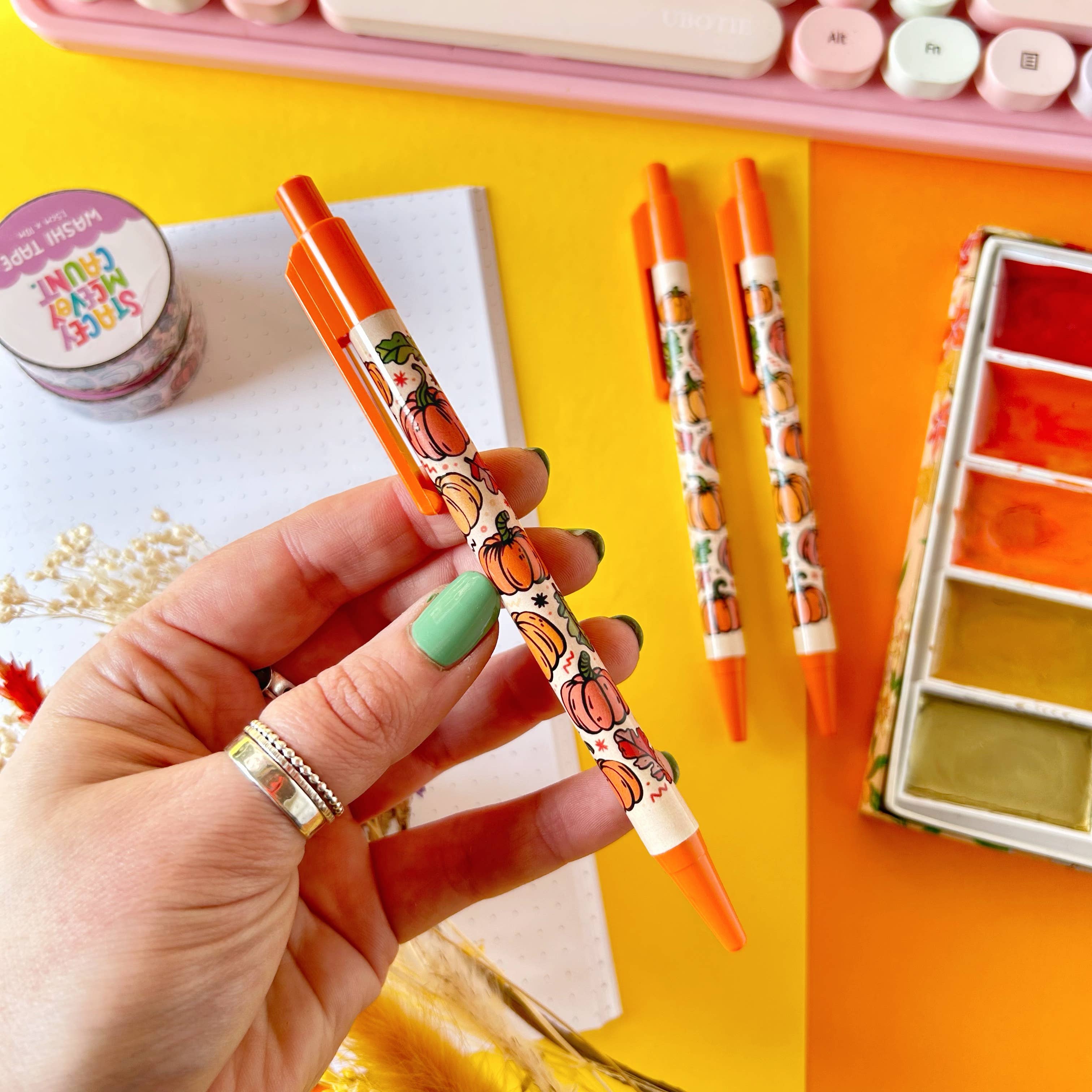 Hand holding a decorative pen with pumpkins on an orange background