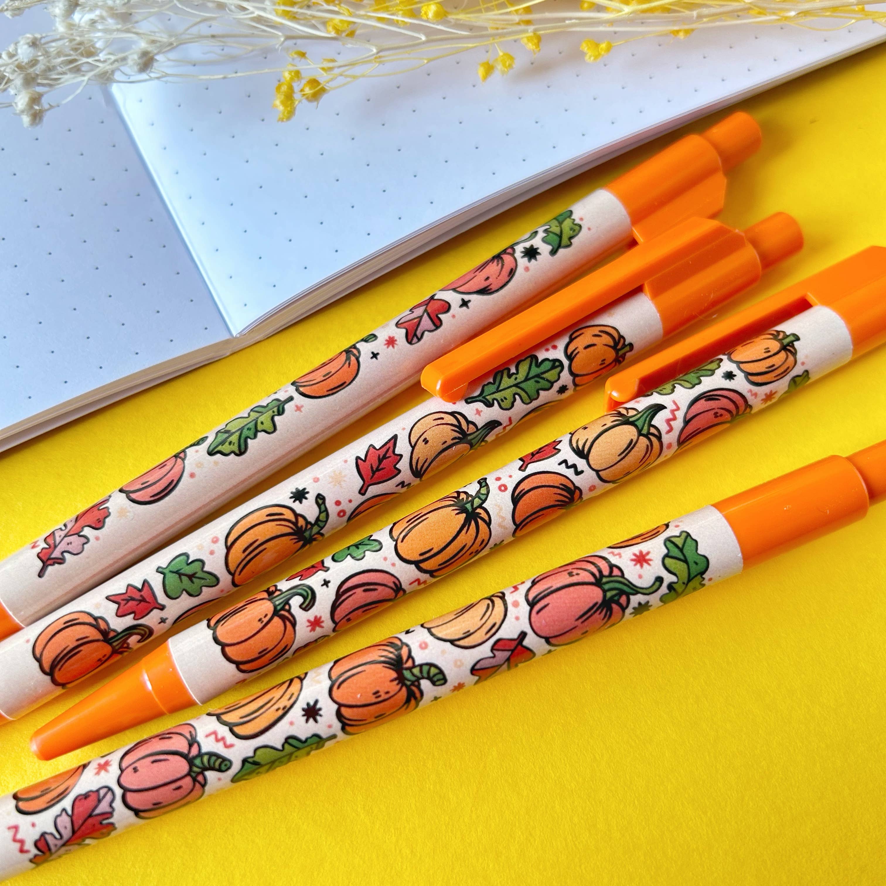 Four pens with pumpkin and leaf designs on a yellow surface.