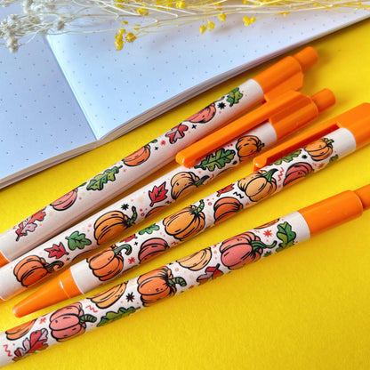 Four pens with pumpkin and leaf designs on a yellow surface.