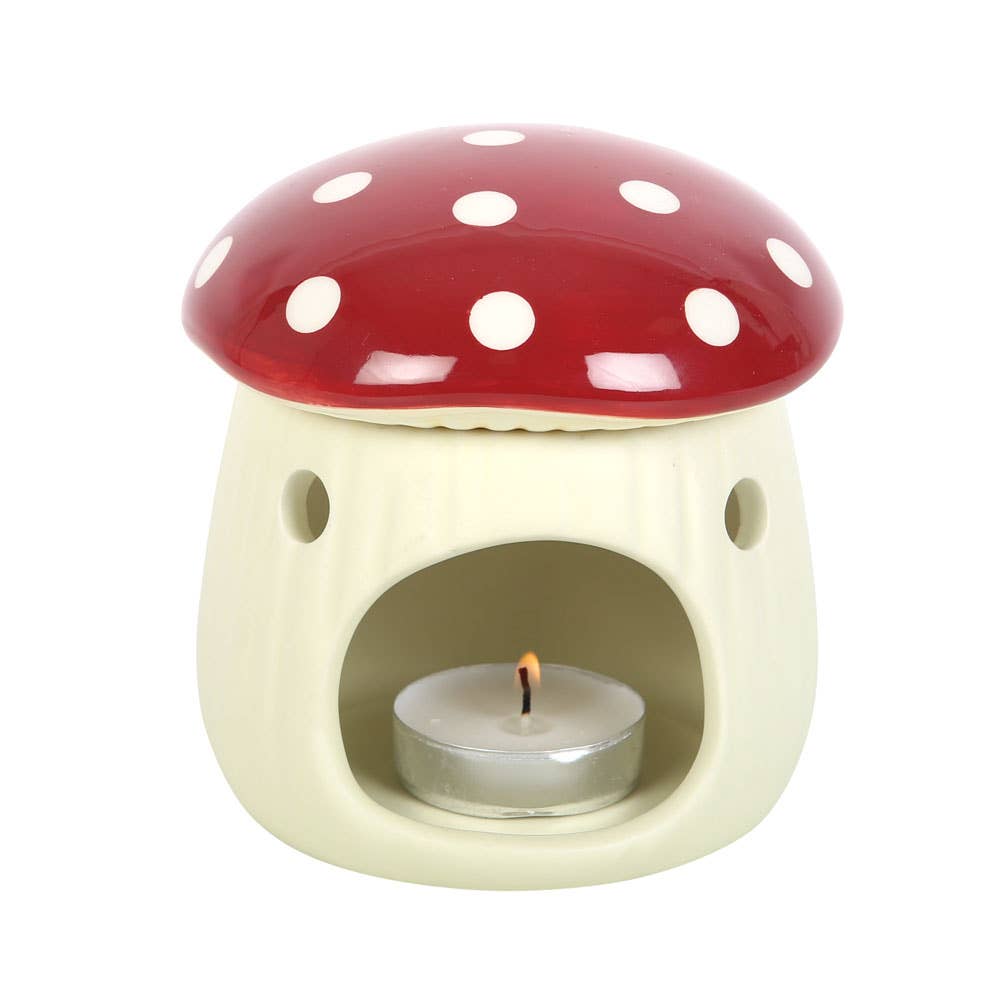 Mushroom-shaped ceramic oil burner with a red cap and white spots, featuring a lit tealight candle inside.