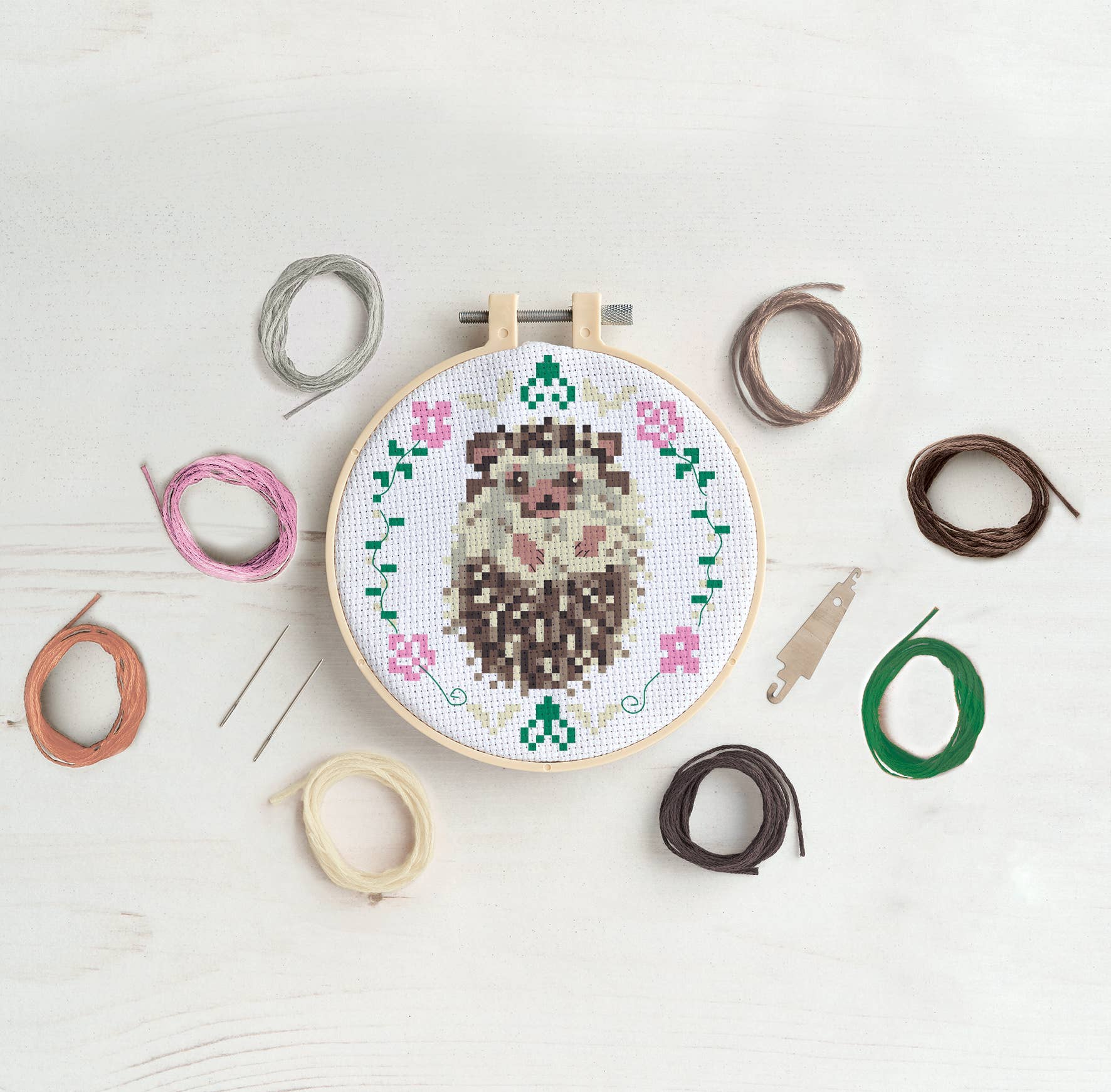 Cross-stitch hoop with a hedgehog design on a white surface with embroidery threads.