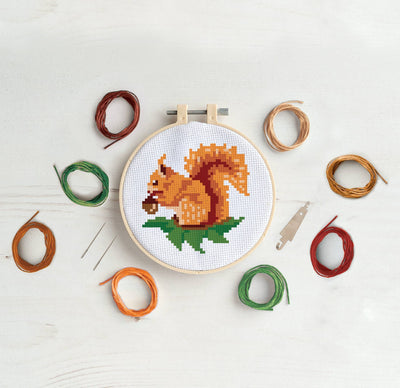 Cross-stitch hoop with a squirrel design surrounded by colored threads on a light surface