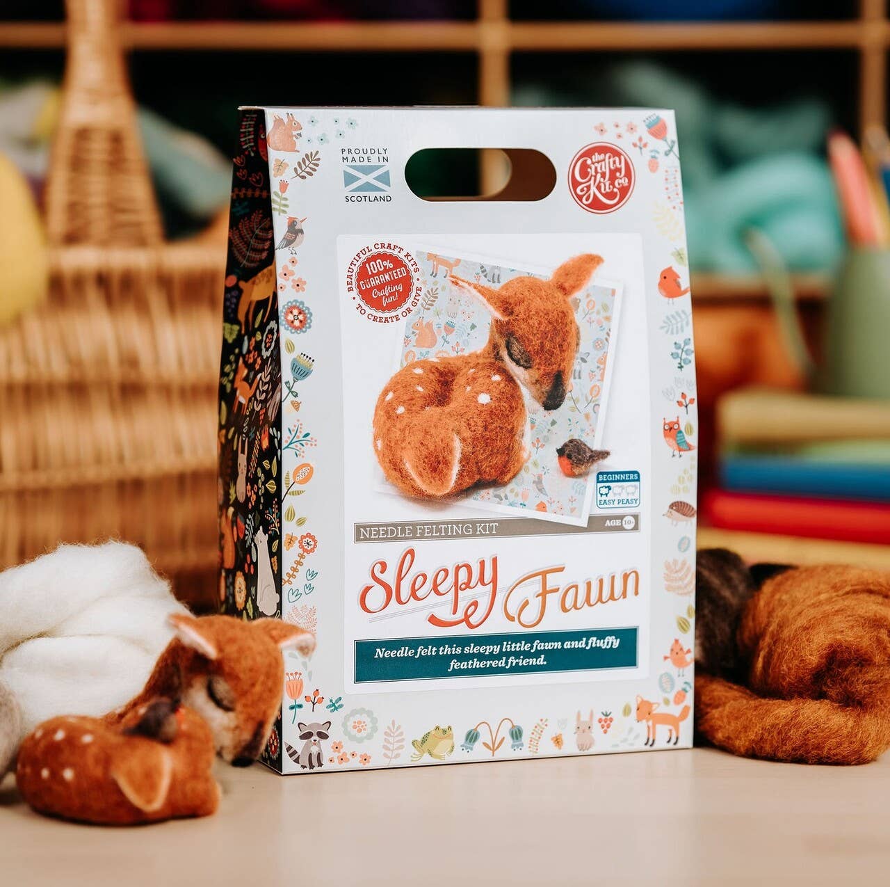 Sleepy Fawn needle felting kit packaging on a table with felted deer and yarn.