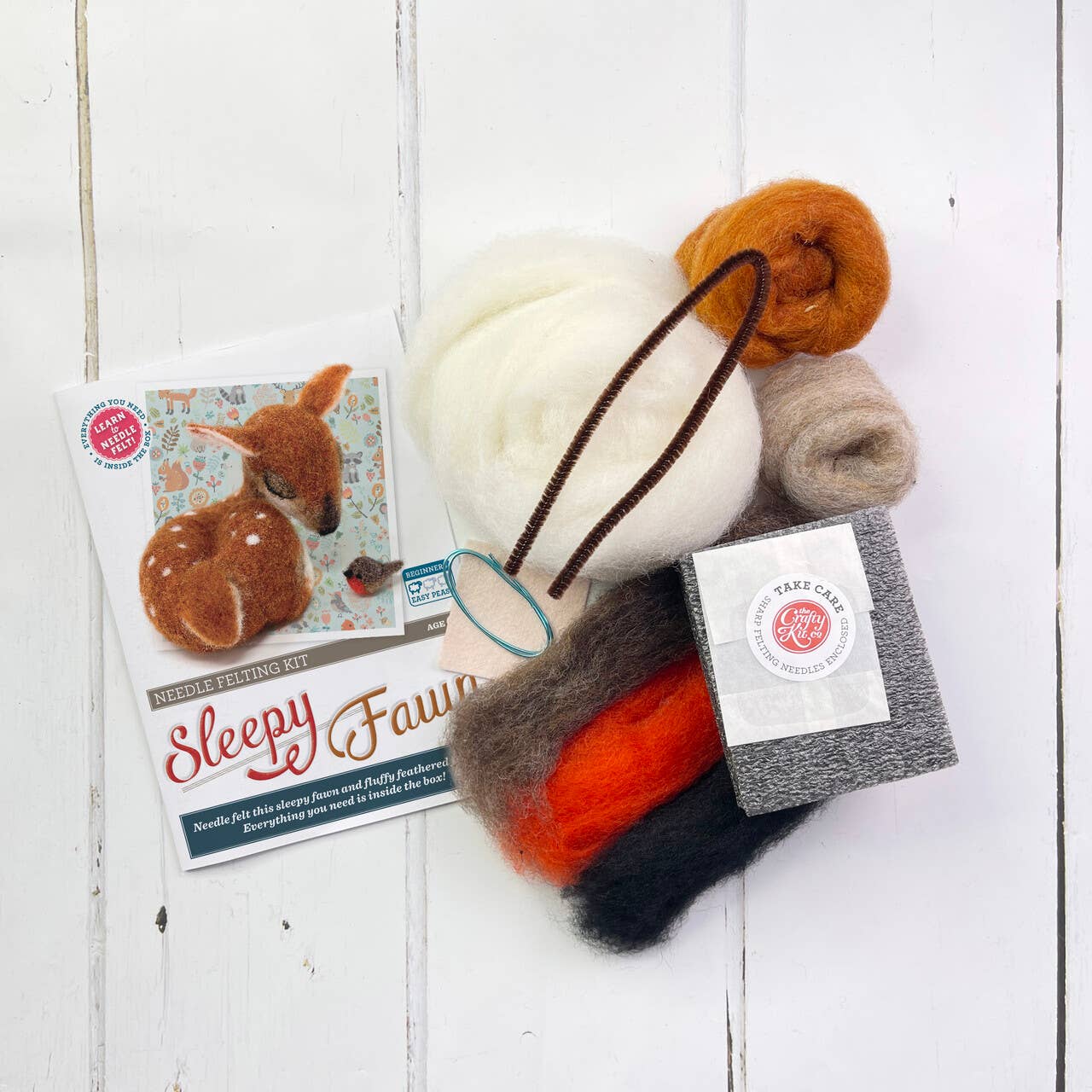 Felted toy deer with needle felting kit on a white wooden surface