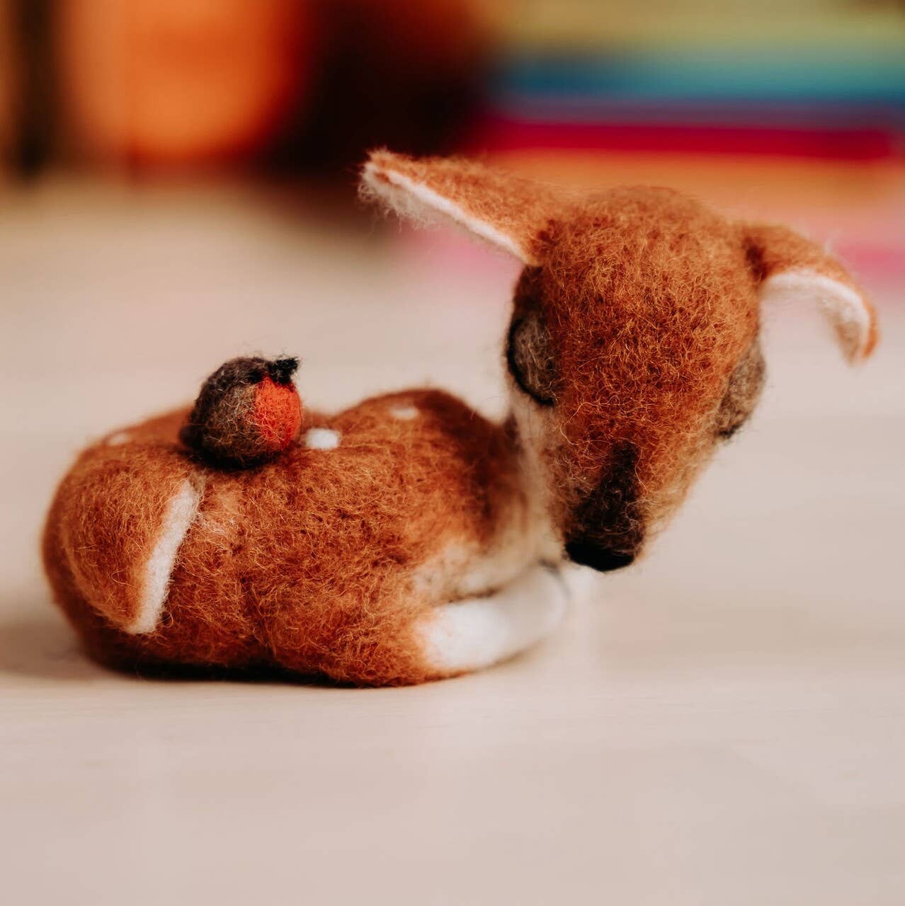 Felted animal figurines of a deer and a bird on a soft surface.
