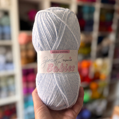 Stylecraft Ball of yarn labeled 'Special for Babies' held in front of a colorful yarn shelf.